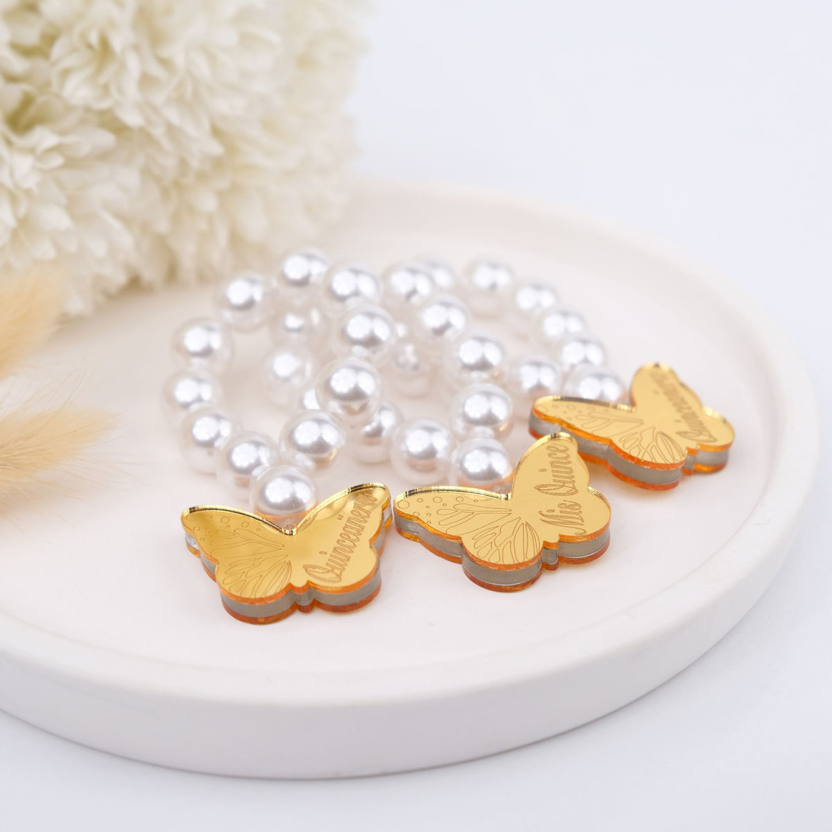 Gold butterfly-shaped party favors on a pearl bead mini rosaries with a white background