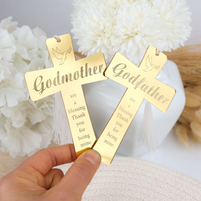 Gold crosses engraved with 'Godmother' and 'Godfather' cross gift held by a hand against a floral background.
