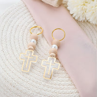 Pair of keychains with cross designs and beige beads on a textured surface.