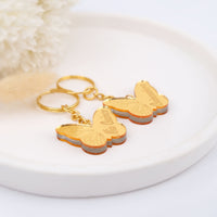 Gold butterfly-shaped keychains on a white surface mis xv favors