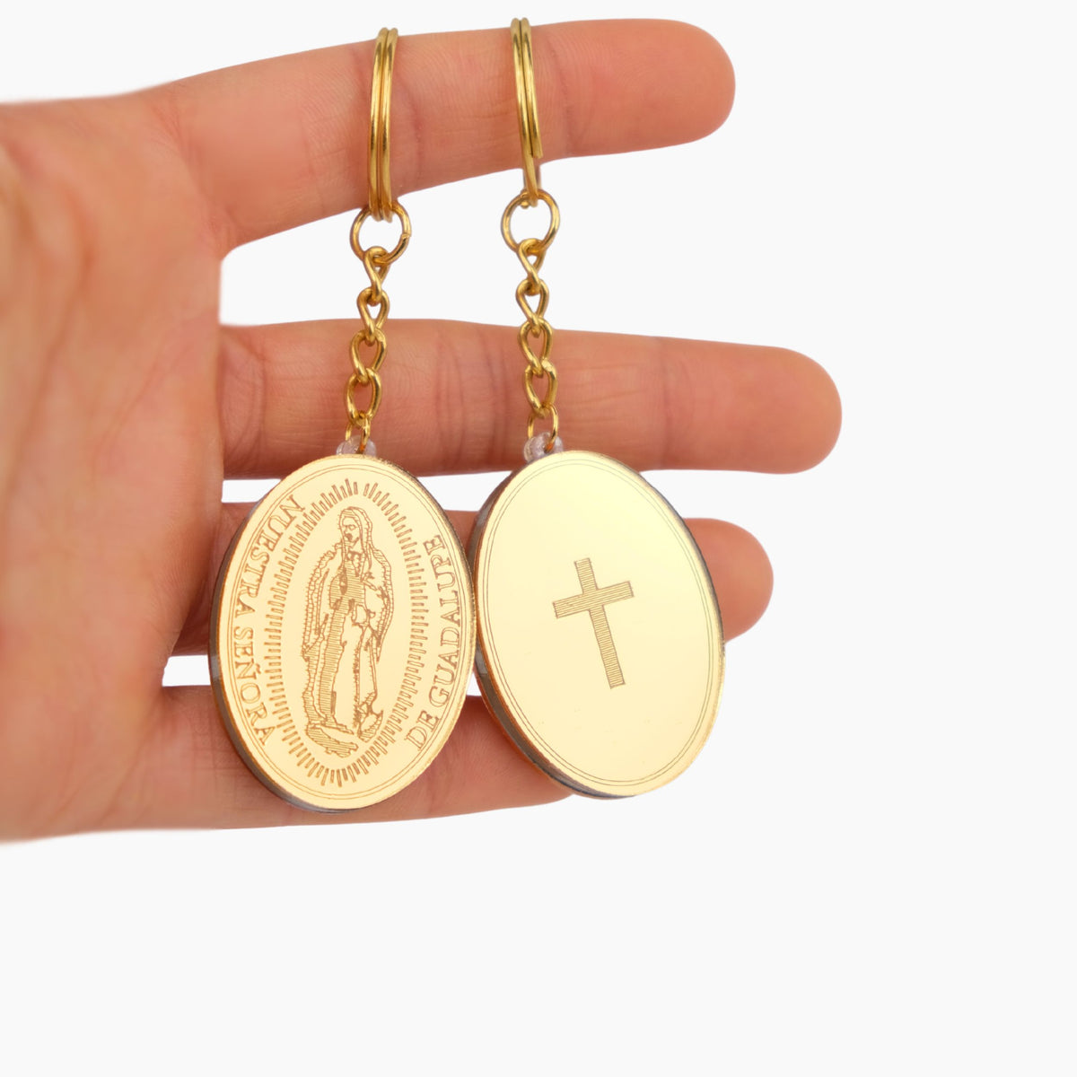 Gold keychain favors oval pendants with religious designs held in a hand against a white background
