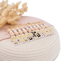 Keychain favors with gold and white cross pendants on a textured surface with dried flowers.