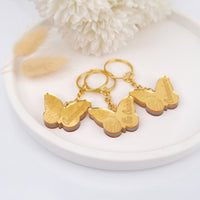 Gold butterfly keychains on a white plate with decorative elements 15th birthday favors