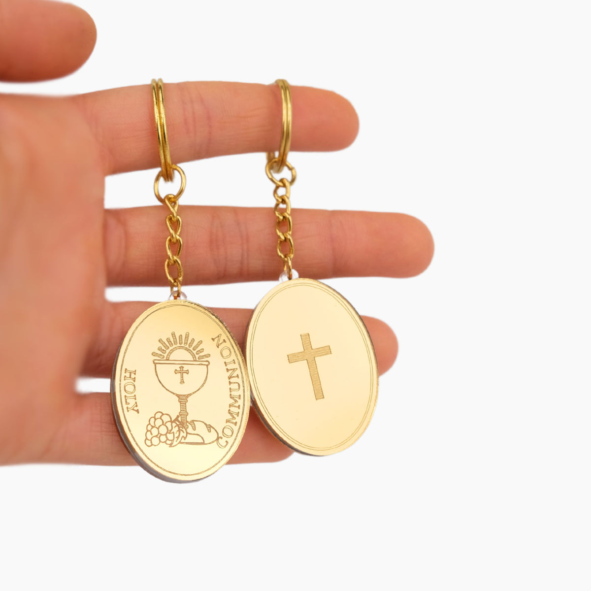 Gold keychain favors with religious designs held in a hand against a white background