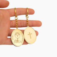 Gold keychain favors with religious designs held in a hand against a white background