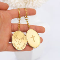 Gold keychain favor pendants with 'GOD BLESS YOU' and cross designs held in a hand against a white background.