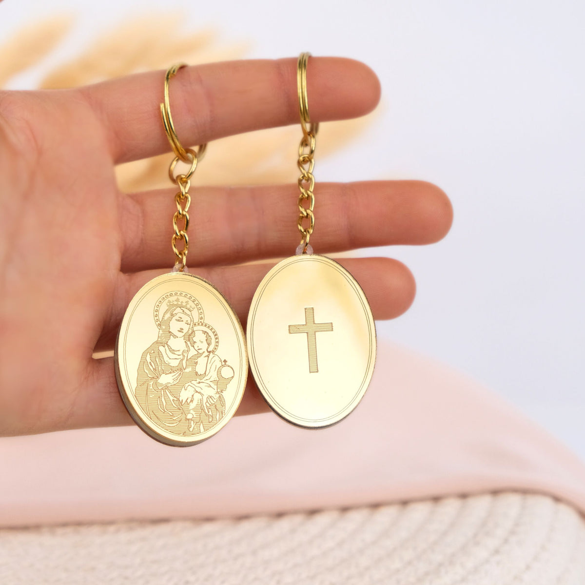 Gold keychain favors with religious designs held in a hand against a light background