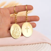 Gold keychain favors with religious designs held in a hand against a light background