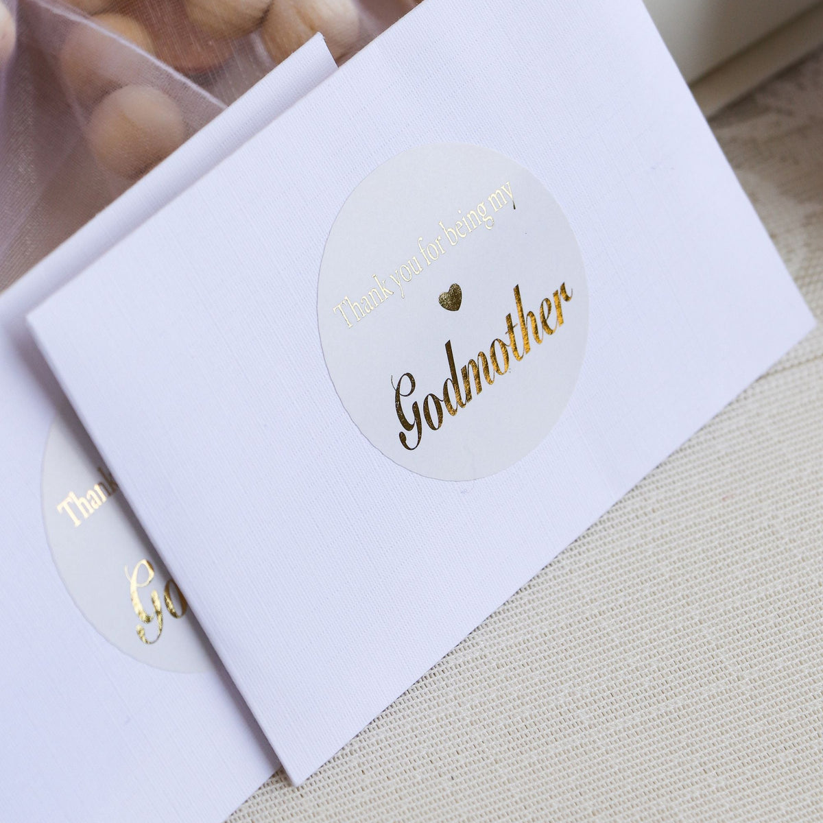 Sticker with 'Godmother' text on a white card, with wooden beads in the background.