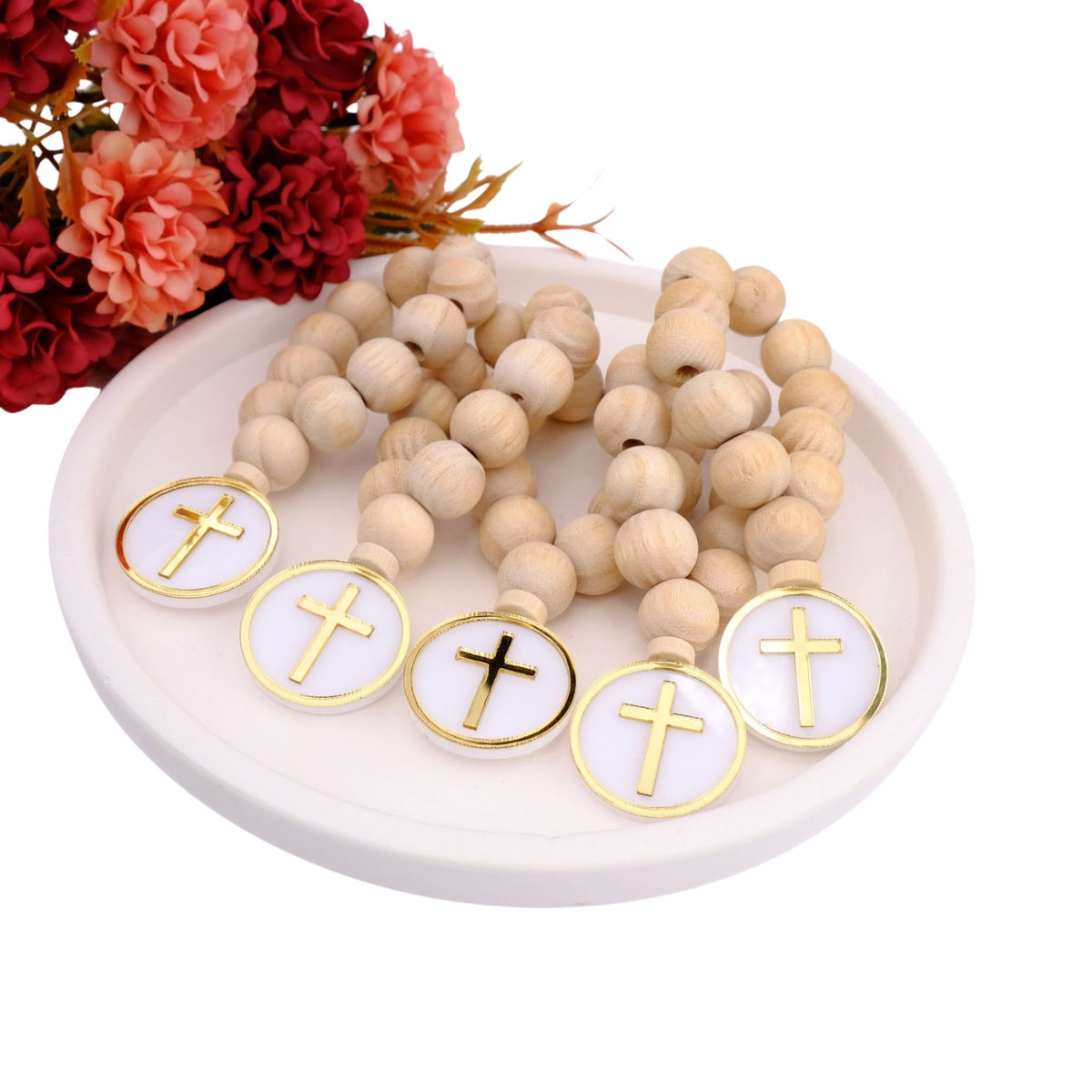 Wooden rosary beads with cross charms on a white plate with flowers in the background