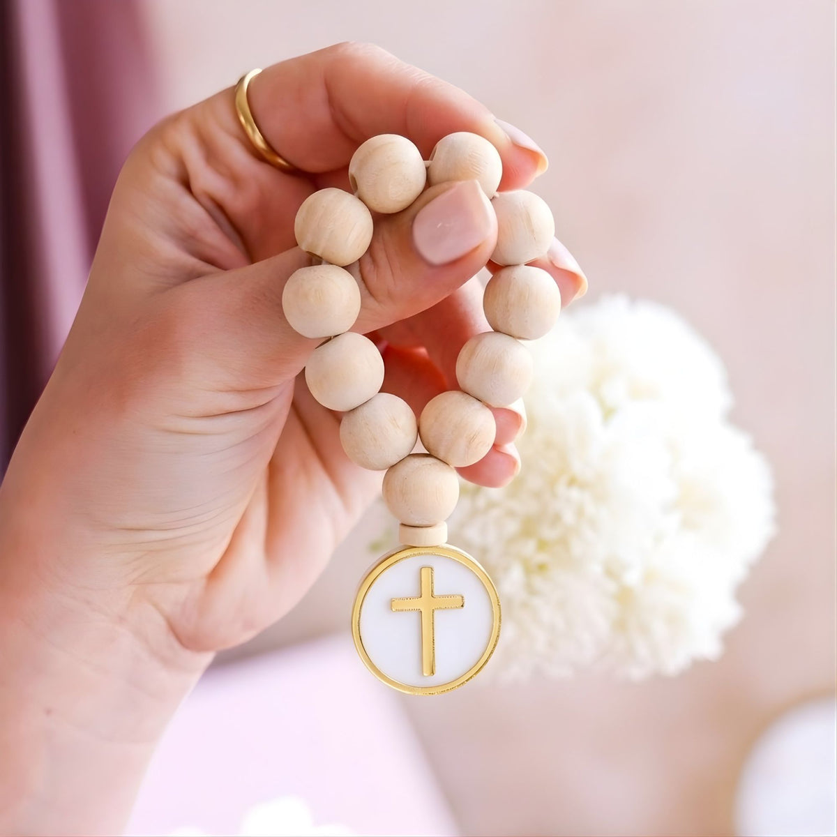Hand holding a wooden rosary with a gold cross charm against a soft background