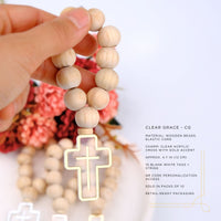 Wooden rosary with clear acrylic cross held by a hand against a floral background