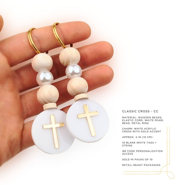 Hand holding a pair of wooden and pearl beaded keychains with gold crosses on a white background.