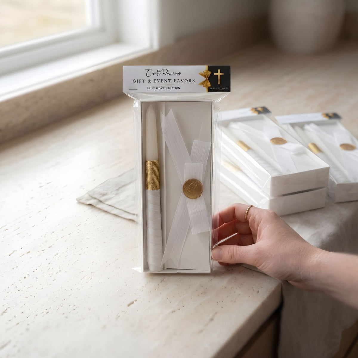 Packaged baptism candle product on a light surface with a hand reaching towards it