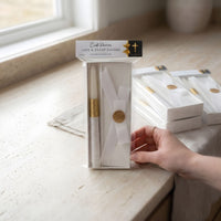 Packaged baptism candle product on a light surface with a hand reaching towards it
