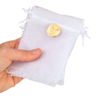 White drawstring bags with gold dove charm held by a hand on a white background