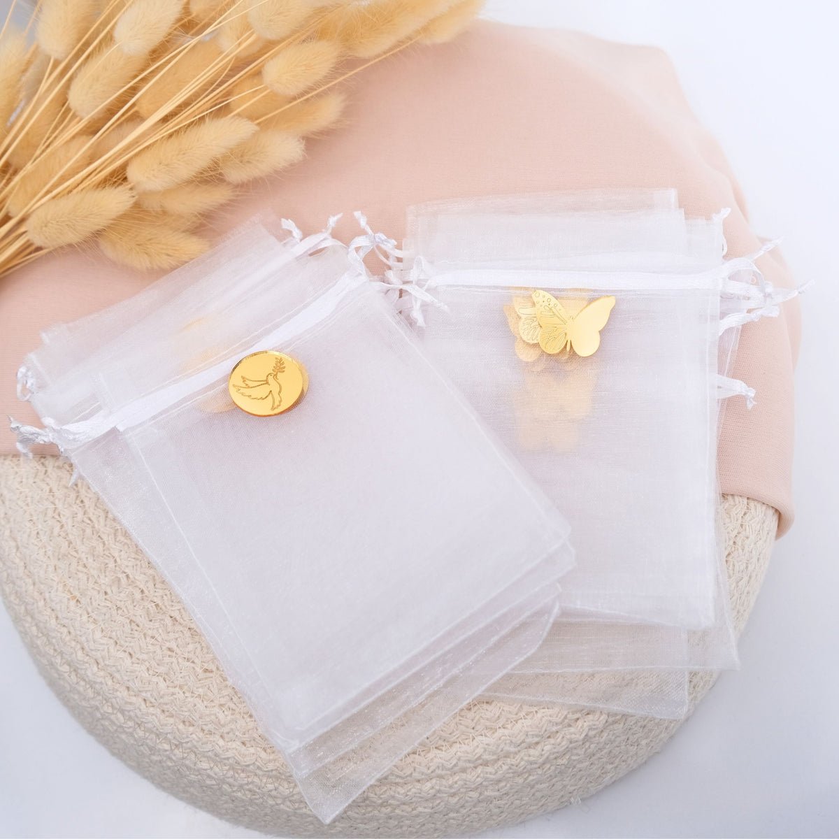 White organza bags with gold butterfly and round charm on a textured surface.