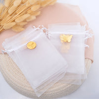 White organza bags with gold butterfly and round charm on a textured surface.