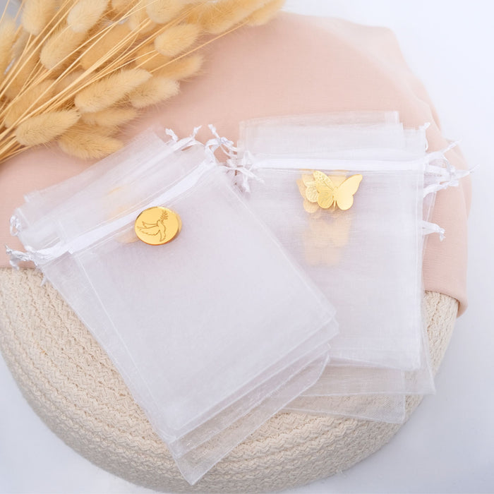 White organza bags with gold butterfly and round charm on a textured surface.