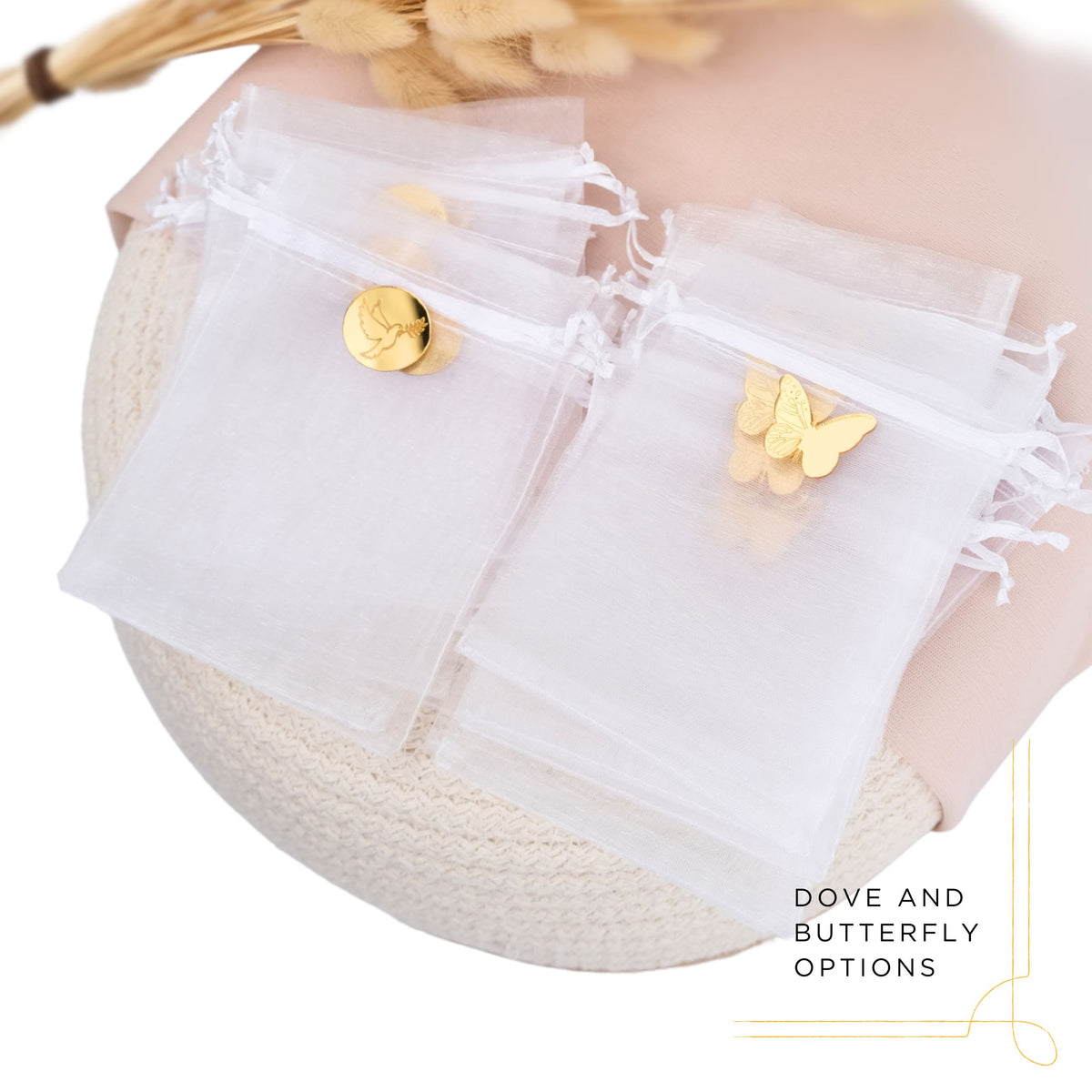 White tulle favor bags with gold charms and butterfly and dove decorations on a neutral background