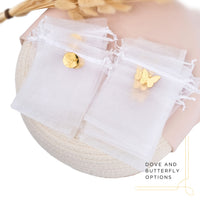 White tulle favor bags with gold charms and butterfly and dove decorations on a neutral background