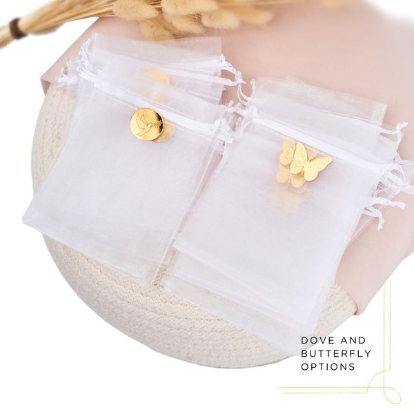 White tulle favor bags with gold charms and butterfly and dove decorations on a neutral background