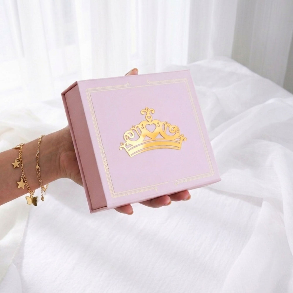 Hand holding a pink box with a gold crown design on a white background