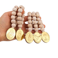 Wooden beaded mini rosary favors with gold religious medallions held by a hand on a white background