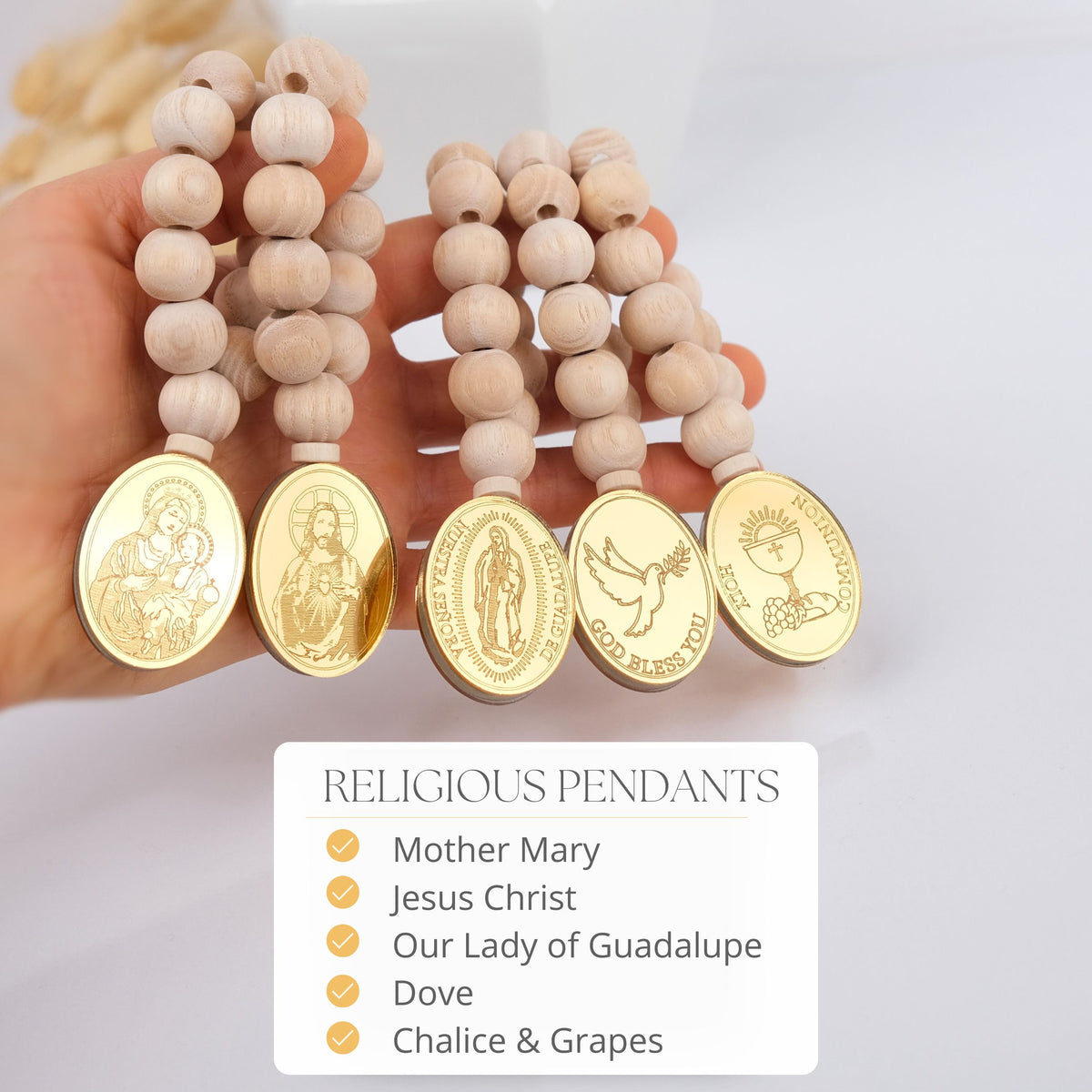 Wooden beaded mini rosaries with gold religious pendants held by a hand, on a light background.