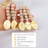 Wooden beaded mini rosaries with gold religious pendants held by a hand, on a light background.