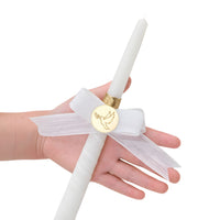 White candle with a gold dove emblem held by a hand on a white background