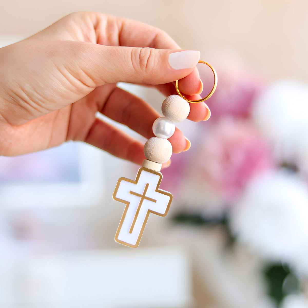 Hand holding a keychain with a cross pendant against a blurred background
