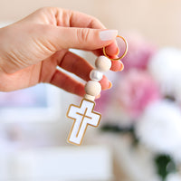 Hand holding a keychain with a cross pendant against a blurred background