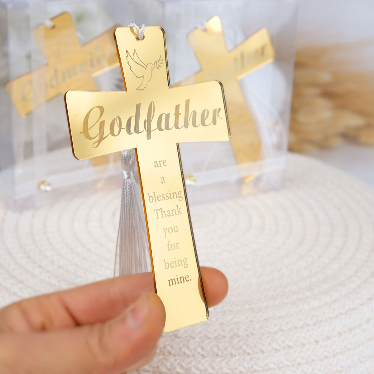 Gold cross pendant with engraved text held by a hand on a white background