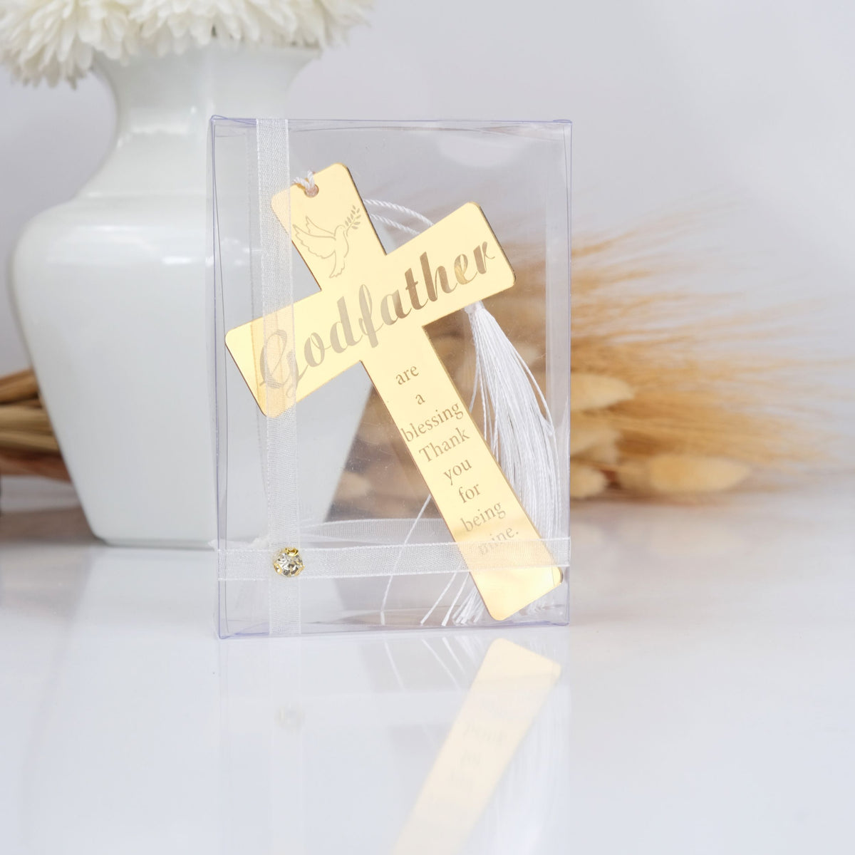 Gold cross with 'Godfather' engraving in a clear packaging on a light background