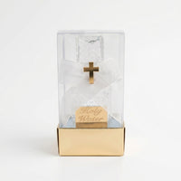 Glass holy water bottle inside a Clear acetate box with decorated design and gold cross on a white background