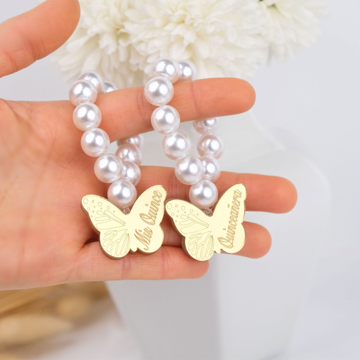 Gold butterfly mini rosaries with 'quinceanera' engraved held against a pearl beads.