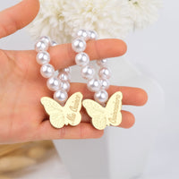 Gold butterfly mini rosaries with 'quinceanera' engraved held against a pearl beads.