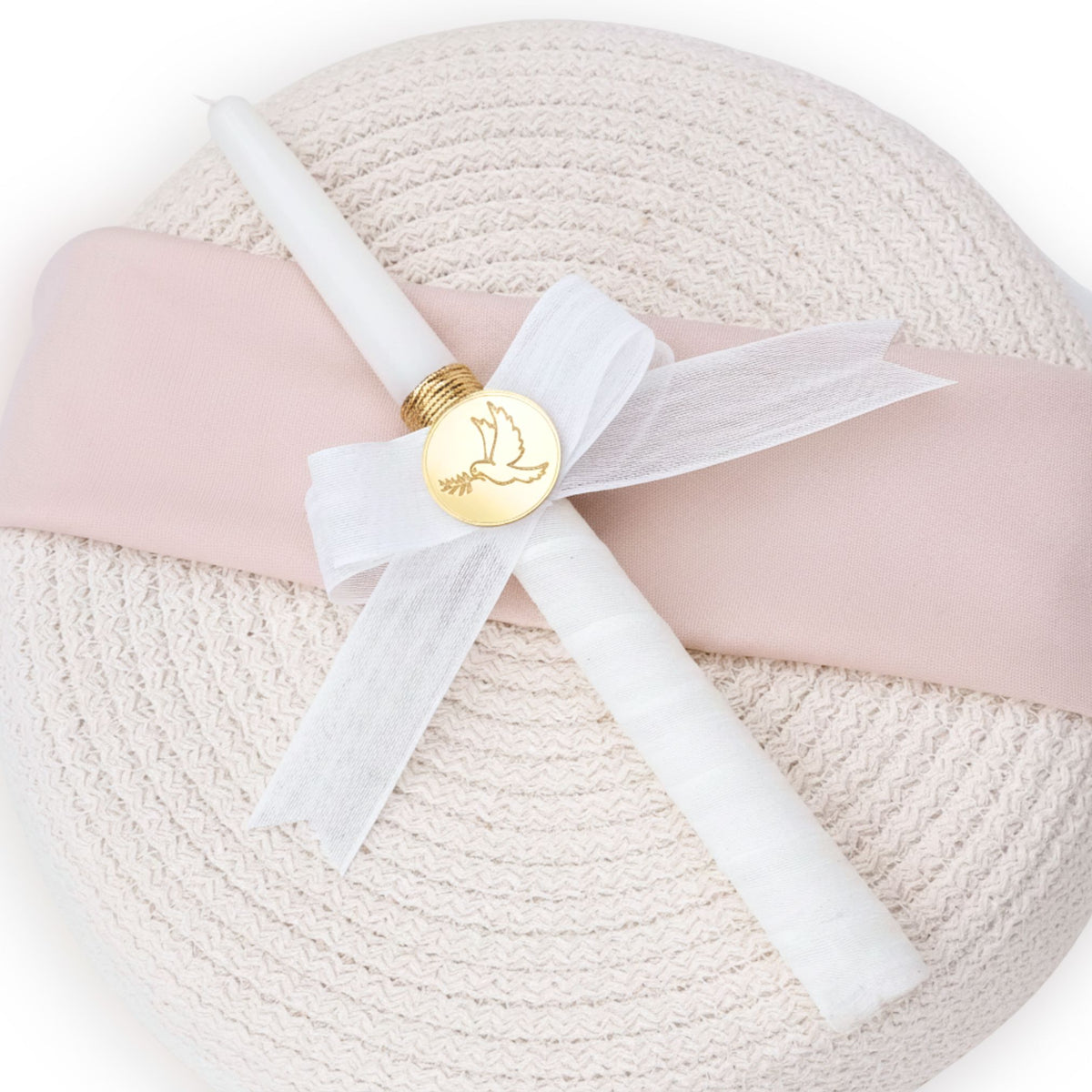 White candle with a gold dove emblem and white bow on a textured pink surface