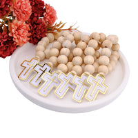 Wooden beaded mini rosary favors with white and gold lettered pendants on a white dish with red and pink flowers.