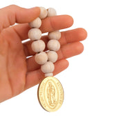 Hand holding a wooden rosary with a Guadalupe figure gold acrylic charm on a white background