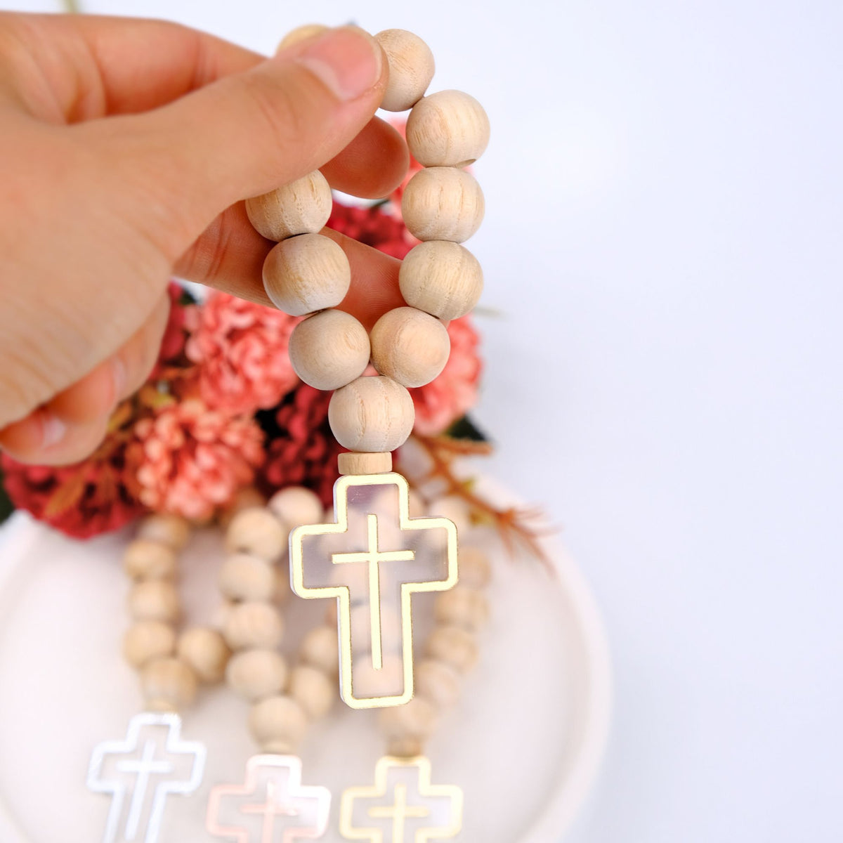Wooden rosary favors with a cross pendant held by a hand against a blurred floral background.