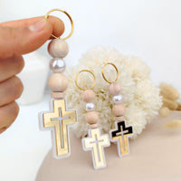 Hand holding a keychain with cross designs and wooden beads against a neutral background