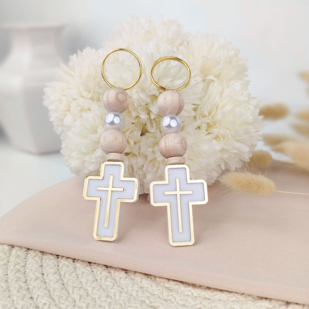 Pair of keychains with cross designs on a soft surface with flowers in the background