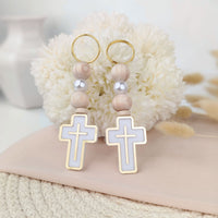 Pair of keychains with cross designs on a soft surface with flowers in the background