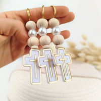 Hand holding a set of baptism keychains with wooden beads and cross designs.