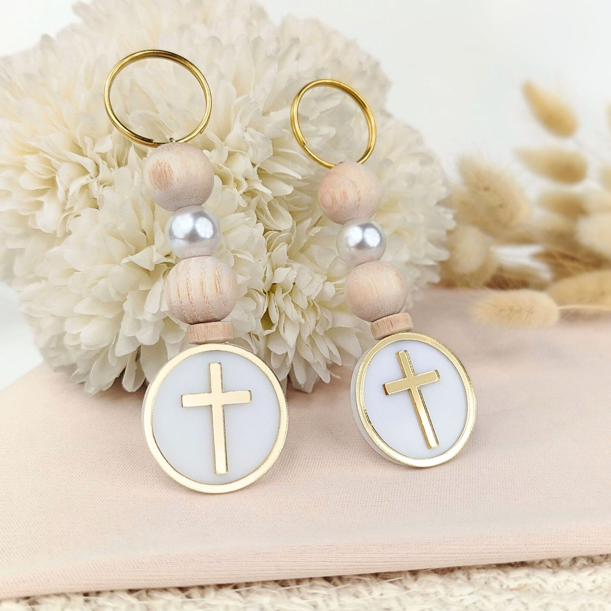 Two baptism favor keychains with wooden beads and gold crosses on a floral background