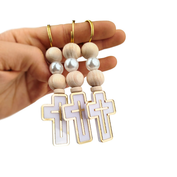 Hand holding a decorative keychain with wooden beads and cross designs on a white background