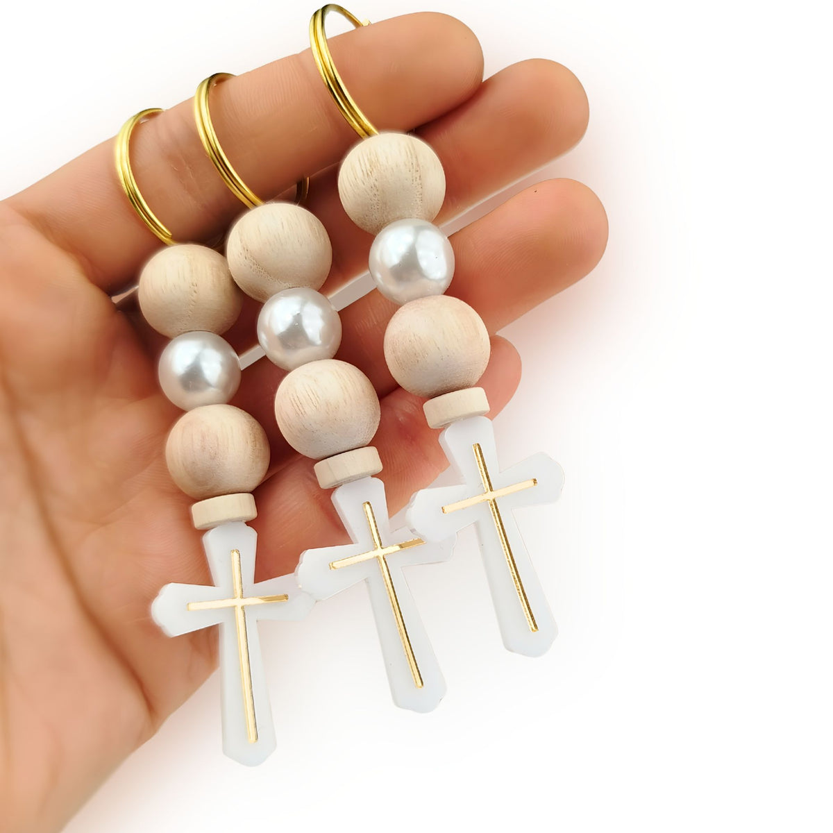 Hand holding a rosary with wooden beads and gold crosses on a white background