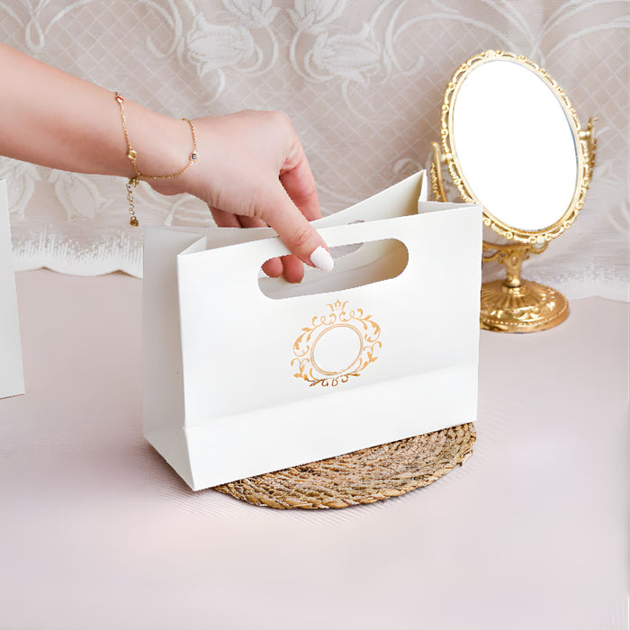 White gift bag with gold details held by a hand, with a decorative mirror in the background.